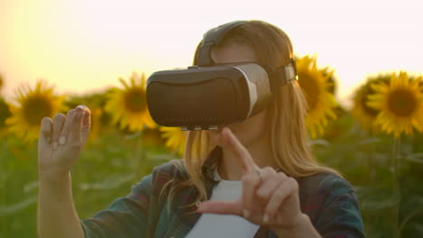 The-young-woman-is-working-in-VR-glasses.-She-is-engaged-in-the-working-process.-It-is-a-perfect-sunny-day-in-the-sunflower-field.